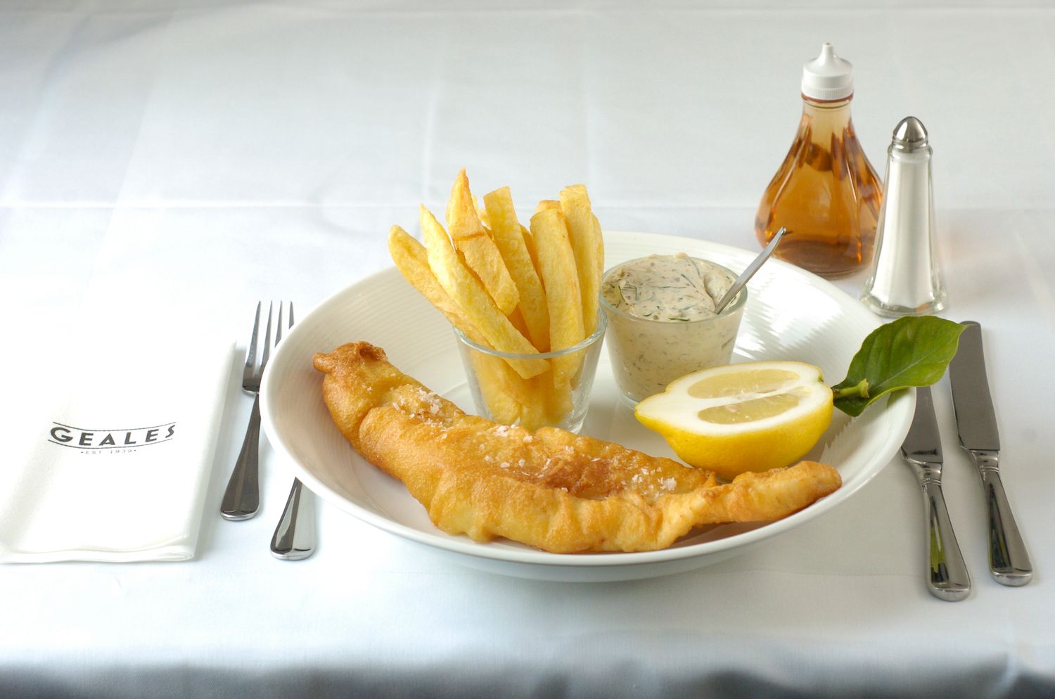 Classic fish and chips with tartar sauce, lemon, and fries on a white plate at Geales restaurant.