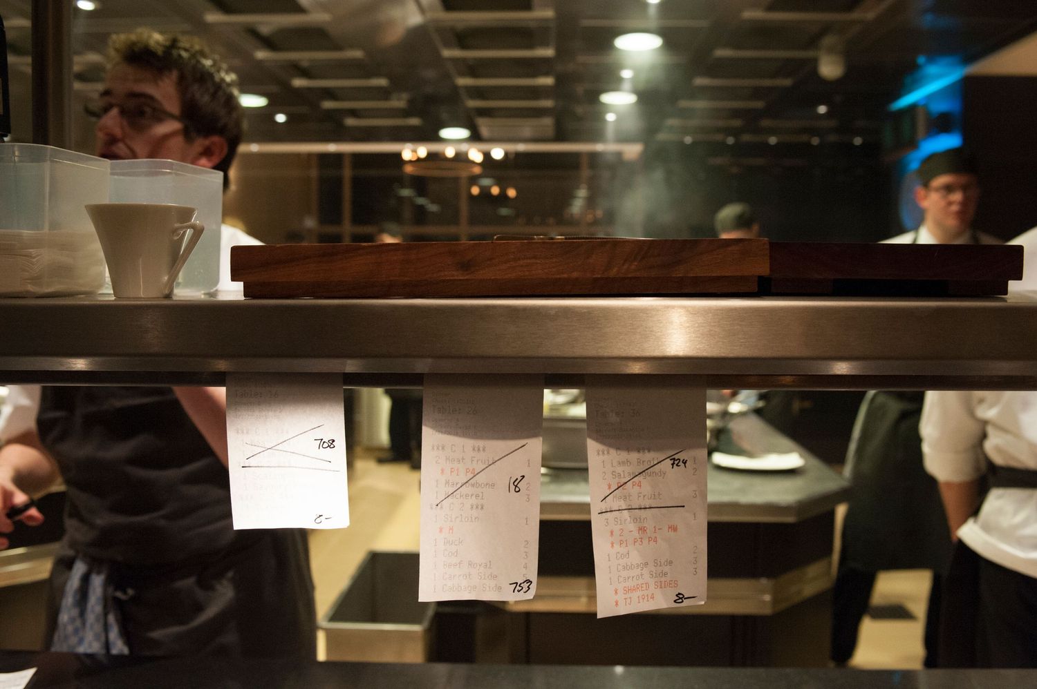 Chef reviewing order tickets clipped below a kitchen pass-through window in a dimly lit restaurant.