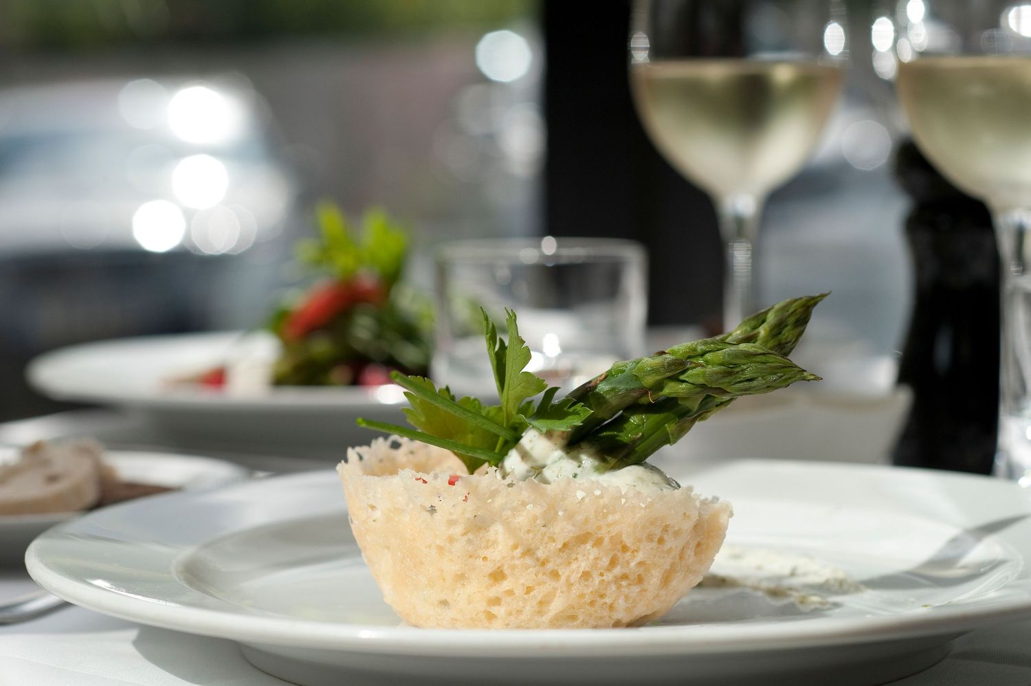 Elegant gourmet appetizer in a parmesan basket topped with asparagus and cream cheese, served on white plate with white wine.