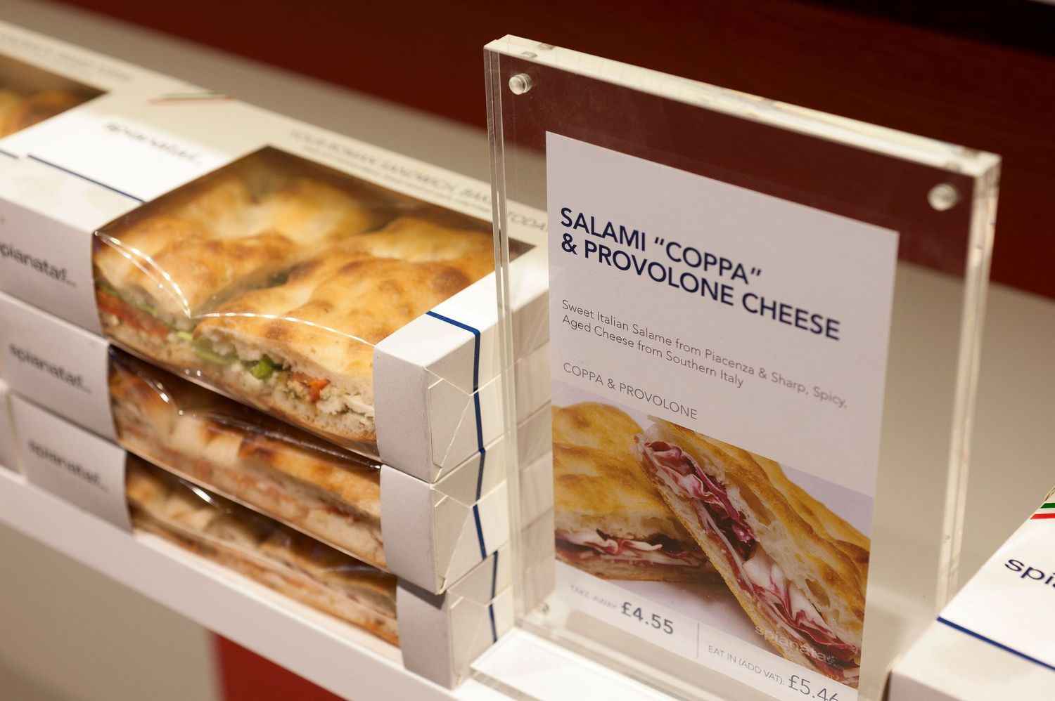 Salami Coppa and Provolone cheese sandwich displayed in a deli case with a menu sign at a cafe.