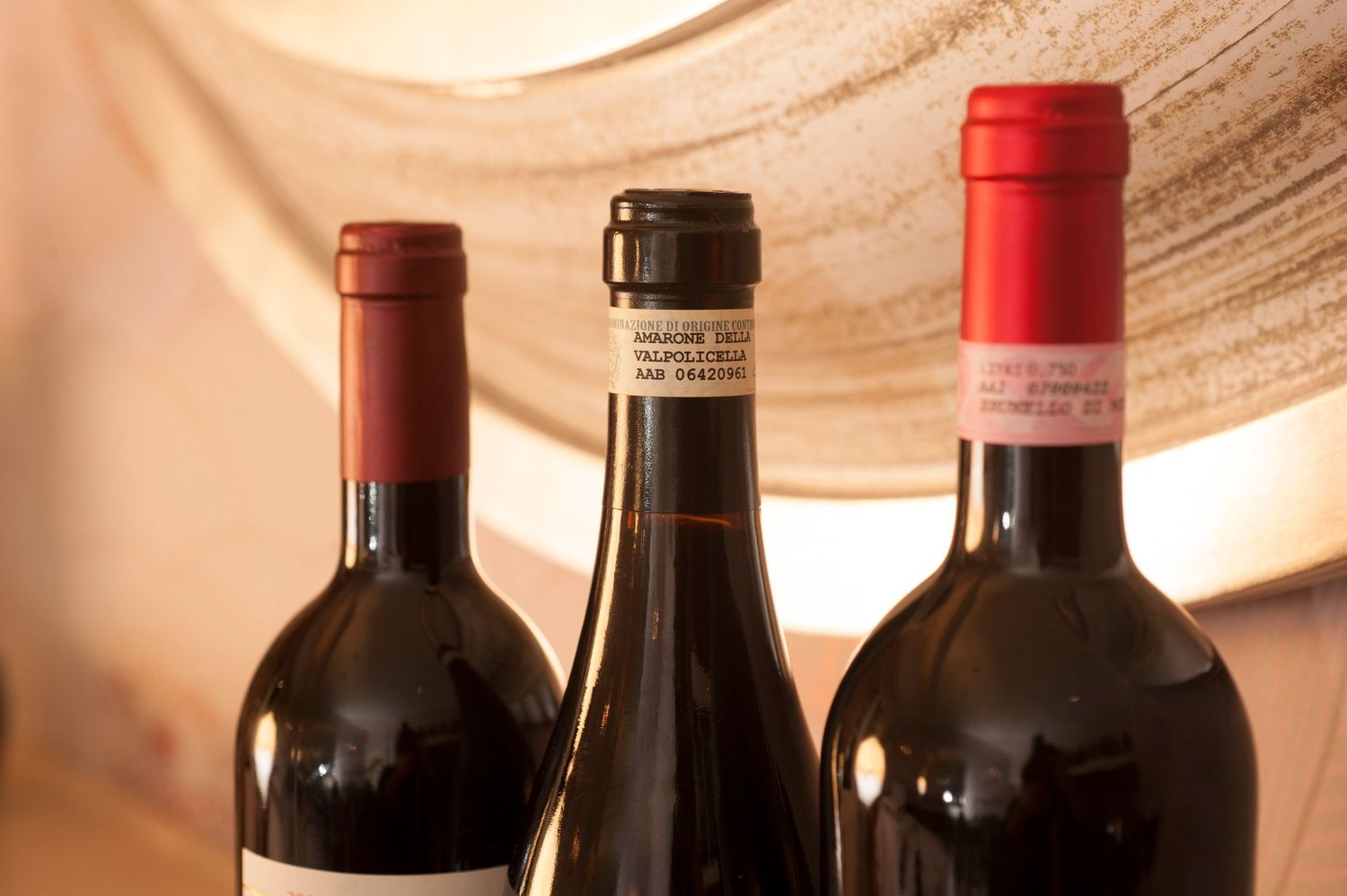 Three dark wine bottles with red caps displayed against a warm glowing background.