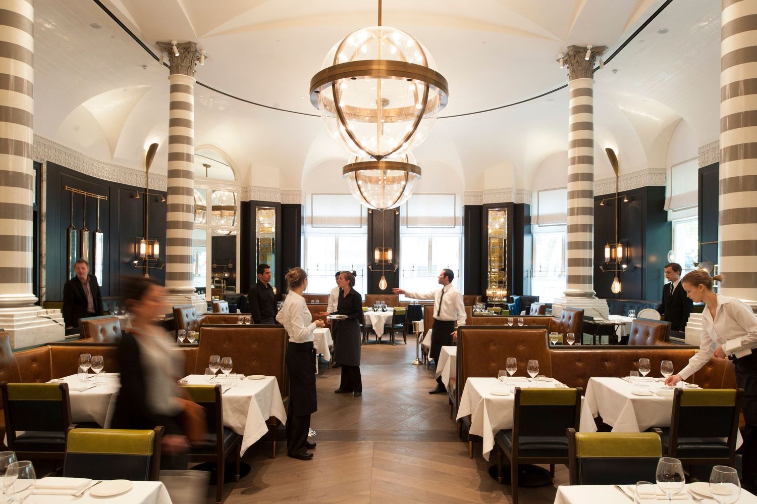 Elegant fine dining restaurant interior with striped columns, white tablecloths, and chandelier lighting.
