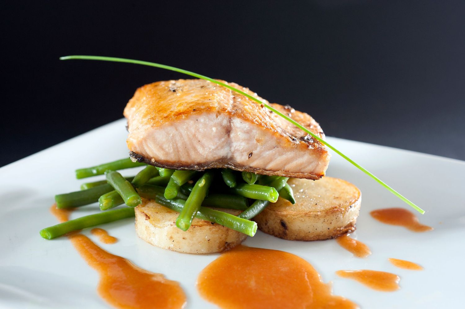 Pan-seared salmon fillet served over green beans and scallops with a rich orange sauce on a white plate.
