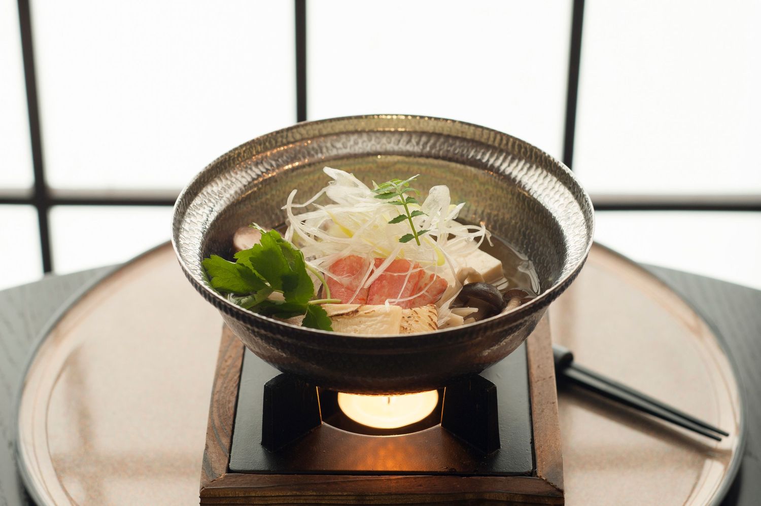 Japanese hot pot dish served in a ceramic bowl on a wooden stand with a lit candle warmer.