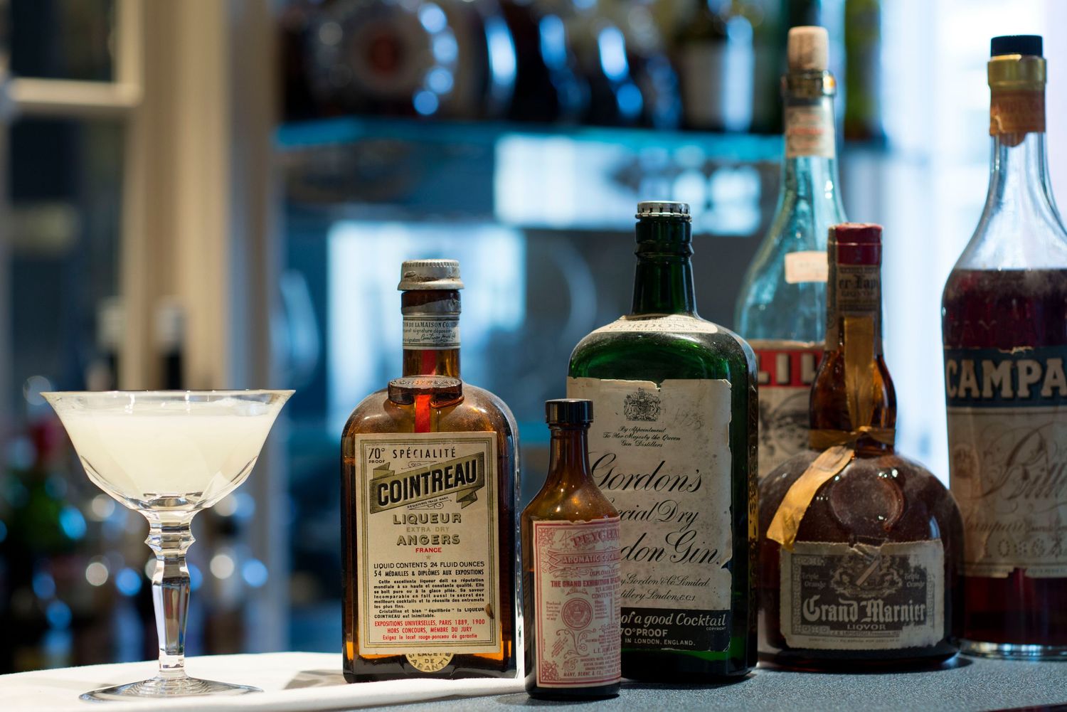 Assorted liquor bottles including Cointreau and Campari displayed on a bar counter with a martini glass.