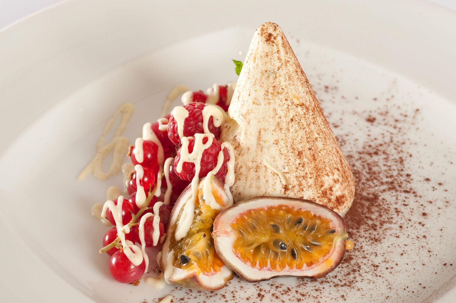 Elegant dessert plate with meringue, fresh raspberries, passion fruit, and cream drizzle dusted with cocoa powder.