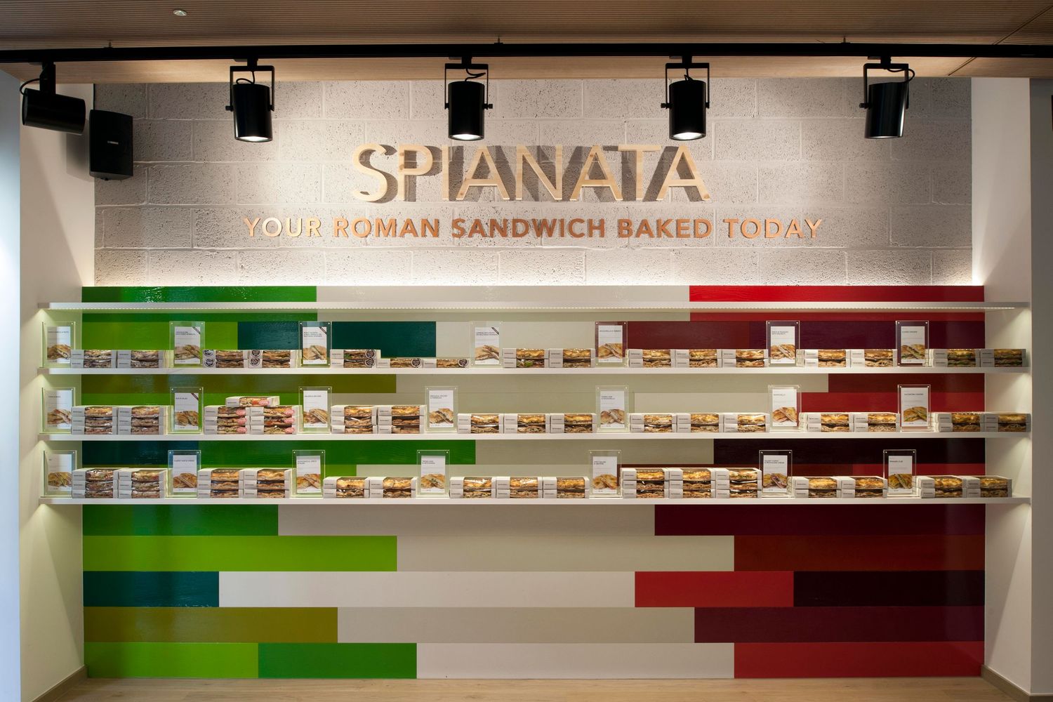 Spianata Roman sandwich shop interior with colorful menu wall display and fresh baked sandwiches on white shelves.