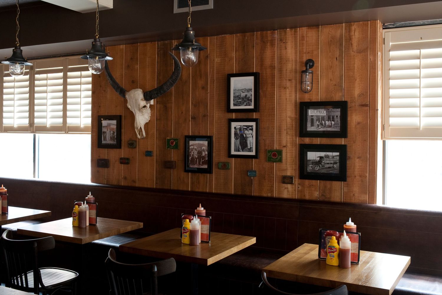 Rustic BBQ restaurant interior with wood-paneled walls, framed photos, mounted antlers, and condiment-topped dining tables.