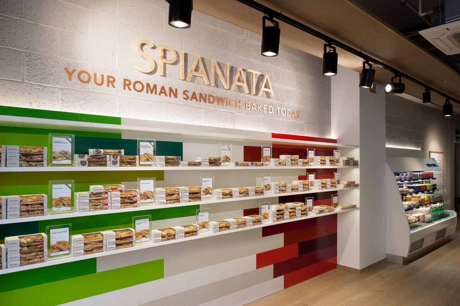 Spianata Roman sandwich shop interior with colorful shelving displaying packaged sandwiches and bright menu boards.