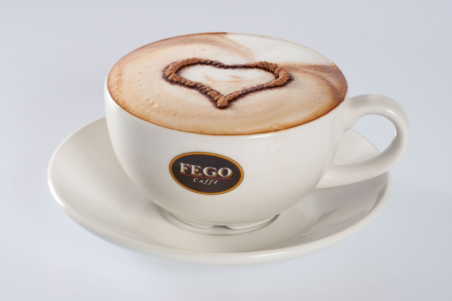 FEGO Caffè cappuccino in a white cup with latte art heart design on frothy milk, served on a matching saucer.