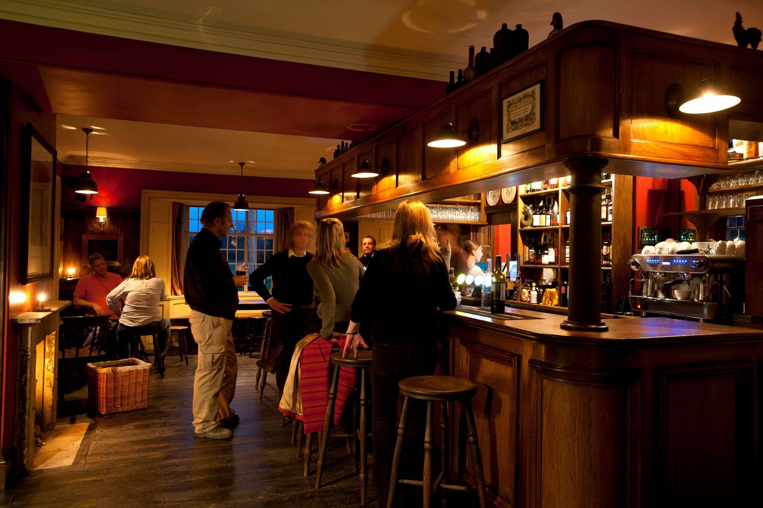 Cozy dimly lit pub bar with wooden stools, warm lighting, and patrons enjoying drinks at the counter.