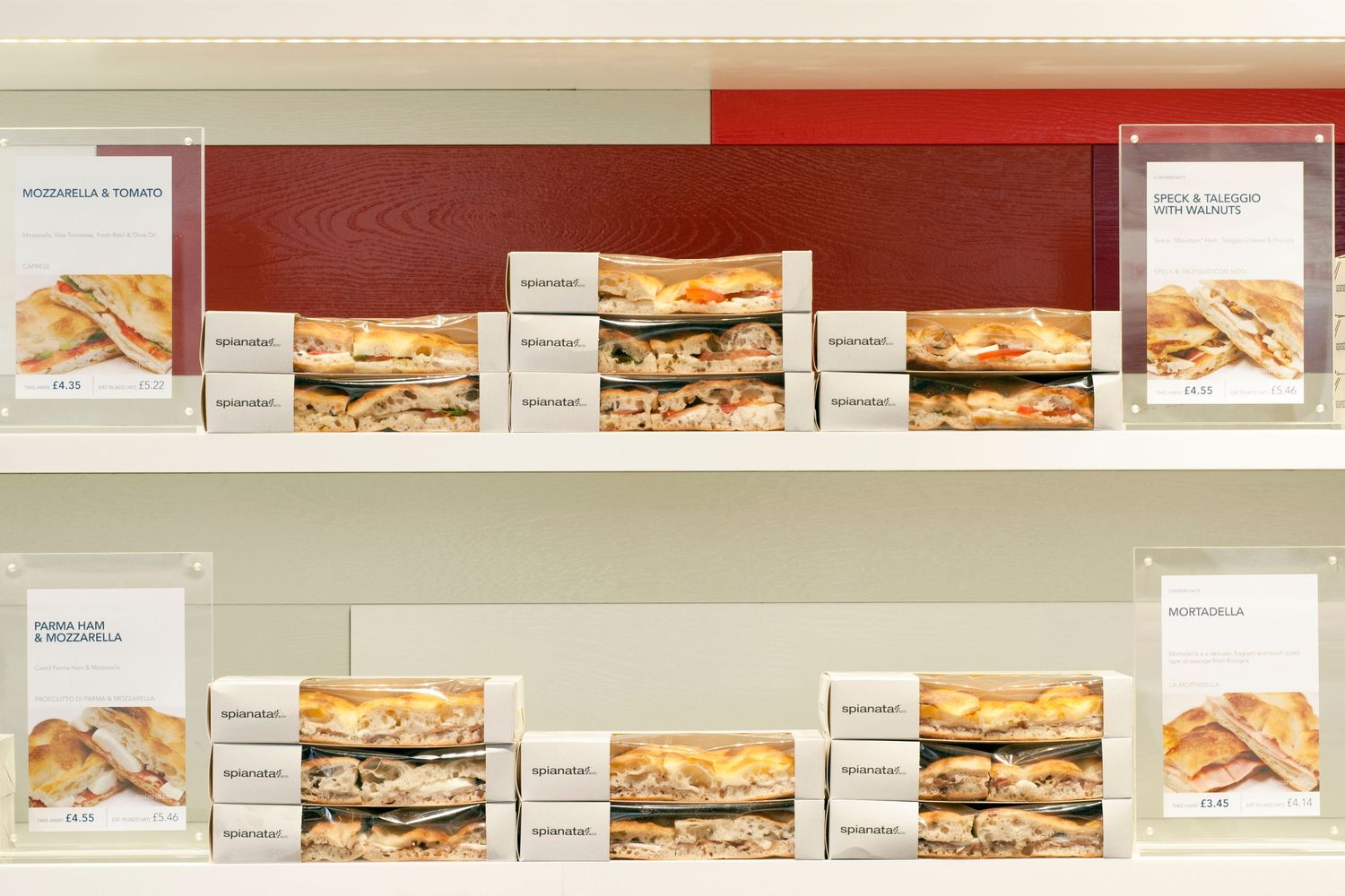 Display shelves showcasing packaged sandwiches with labeled menu cards in a deli or cafe setting.