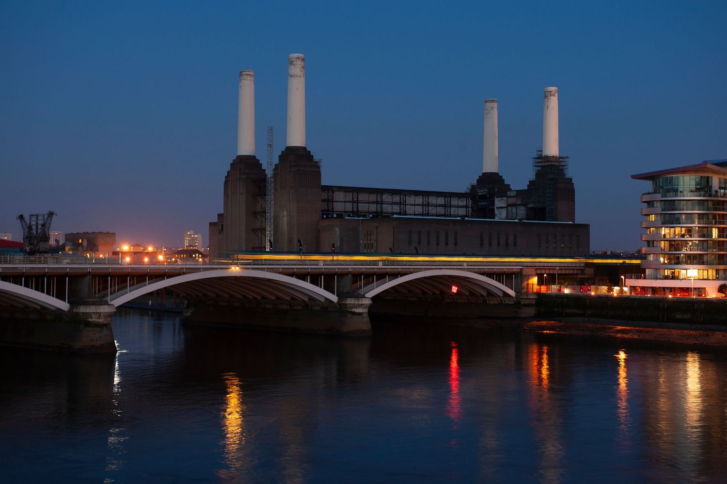 Dusk view of Battersea Power Station chimneys silhouetted against dark blue sky with Chelsea Bridge in foreground.
Photograph by Danny Elwes
