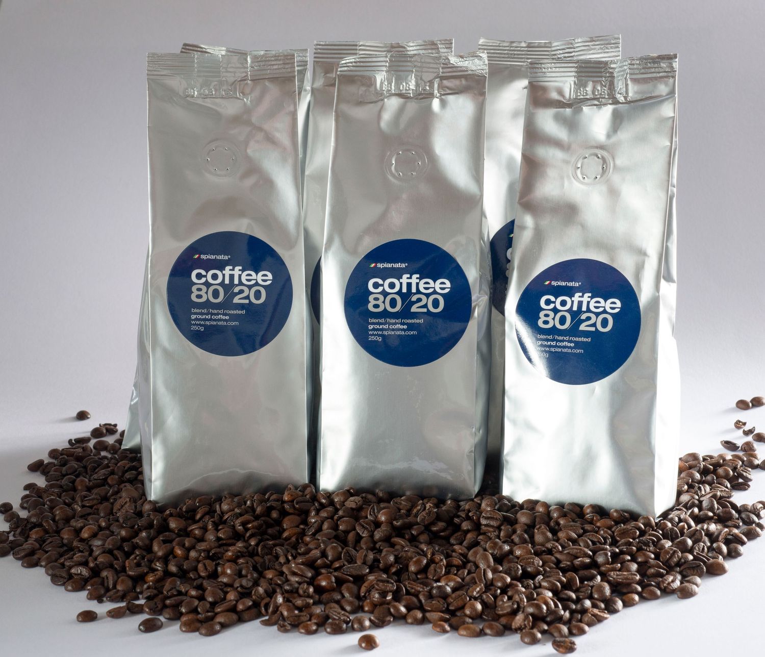 Three silver bags of Coffee 80 20 blend surrounded by roasted coffee beans on a white background.