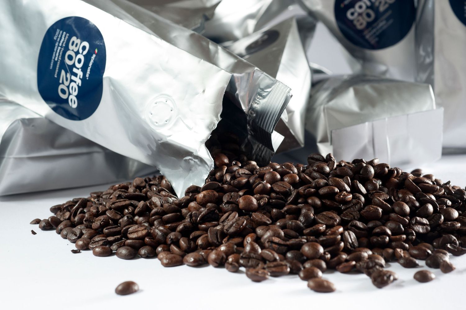 Coffee beans spilling from silver Coffee Co. branded packaging bags on a white surface.
