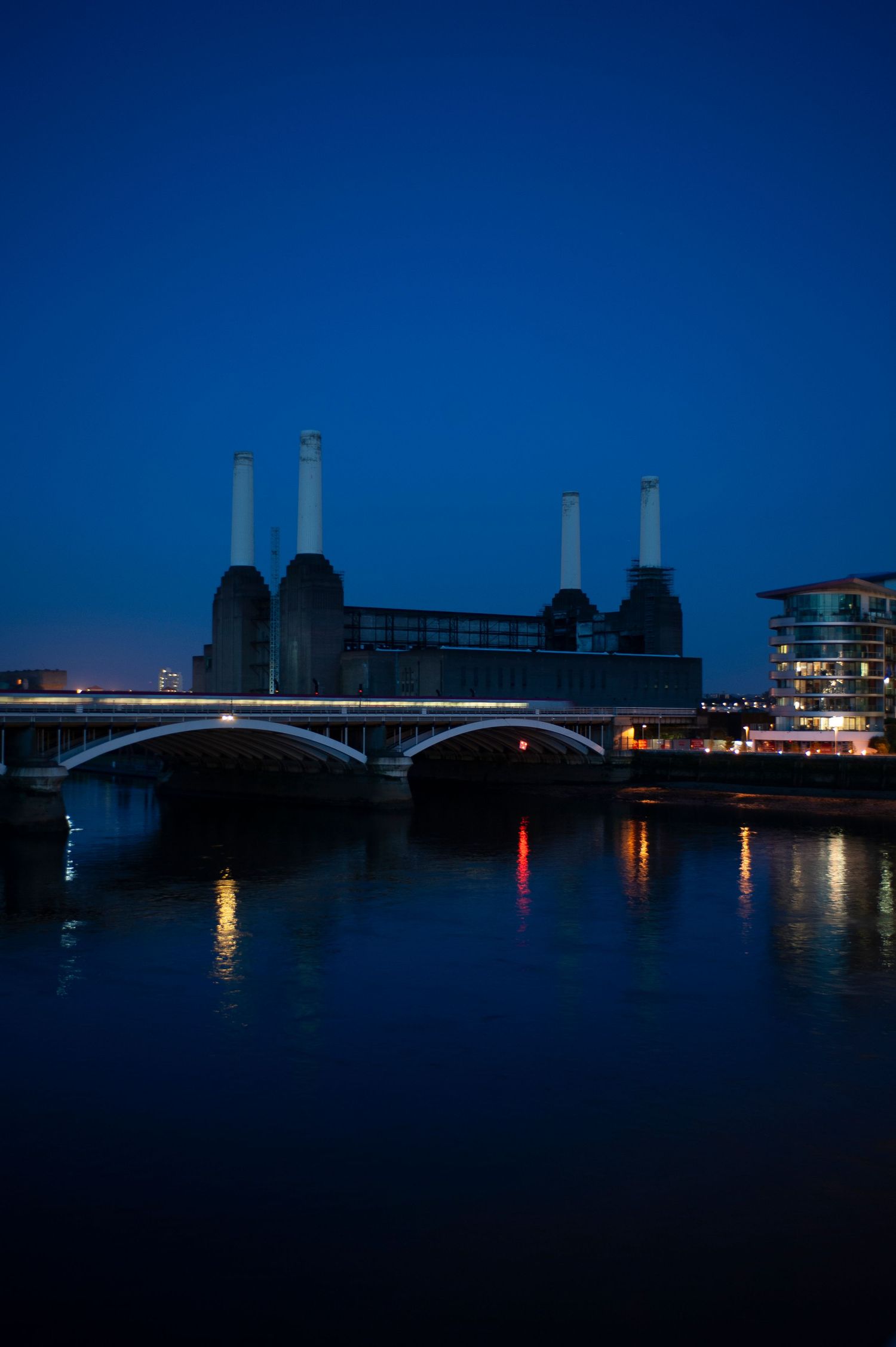 Dusk view of Battersea Power Station chimneys silhouetted against dark blue sky with Chelsea Bridge in foreground.
Photograph by Danny Elwes