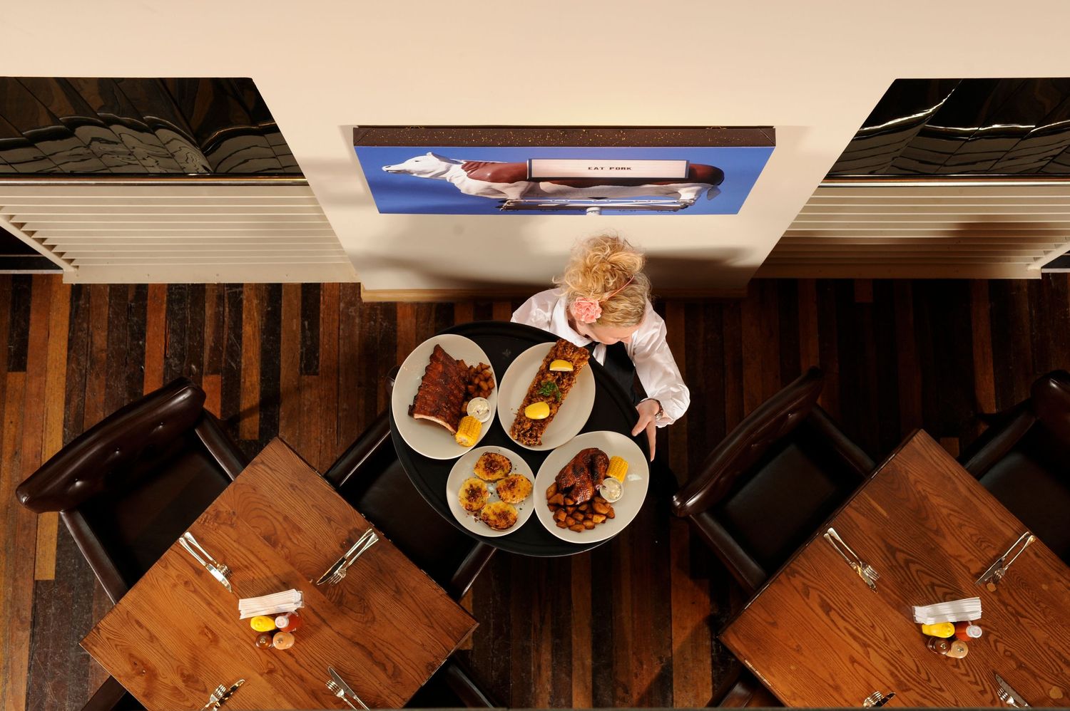 Aerial view of a waiter carrying plates of food to a wooden dining table in a modern restaurant.