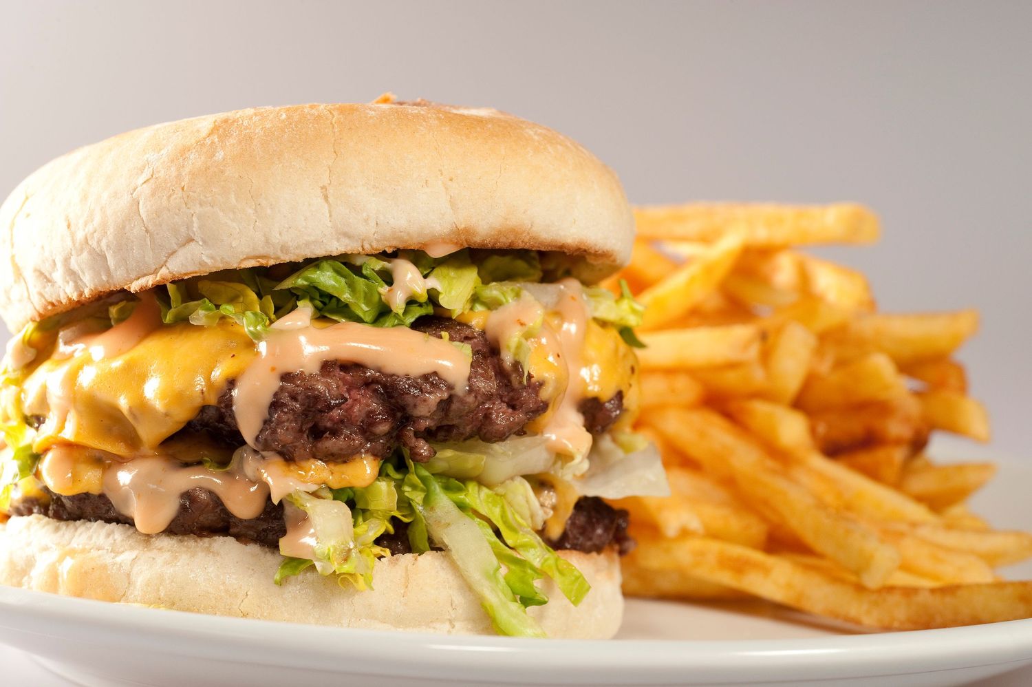 A juicy double cheeseburger with lettuce and special sauce served with golden crispy french fries on a white plate.
