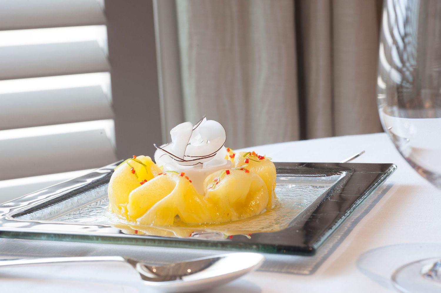 Elegant dessert with pineapple, whipped cream, and red spice on a glass plate in a fine dining setting.