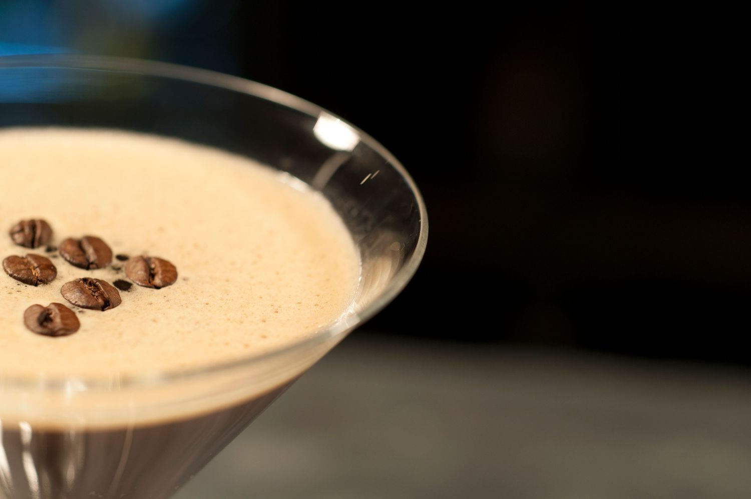 Close-up of a creamy espresso martini in a cocktail glass garnished with three coffee beans on a dark background.