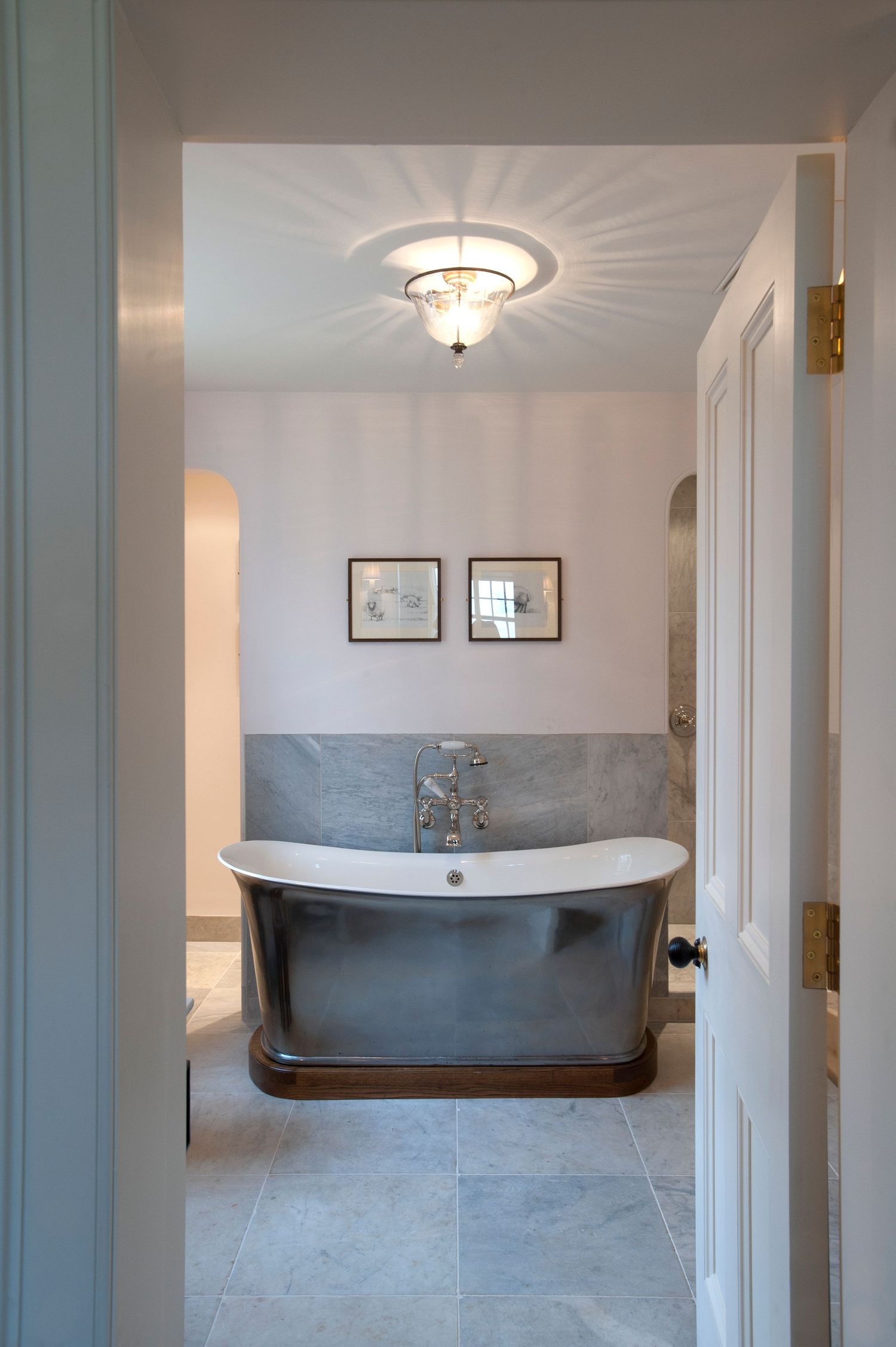 Elegant bathroom with a freestanding metallic clawfoot tub, marble wall tiles, gold fixtures, and a decorative ceiling light.