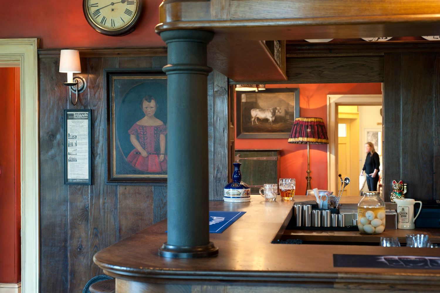 Rustic bar interior with dark wood paneling, vintage portraits, a clock, and warm red walls in a cozy pub setting.