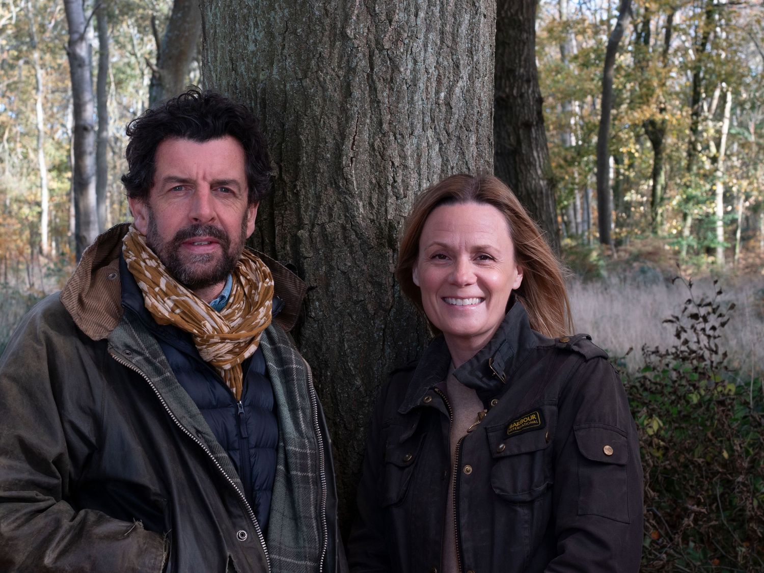 Ross and Michelle for family photograph for 'Before they Fly the Nest (husband and wife) standing beside large tree trunk in autumn forest.