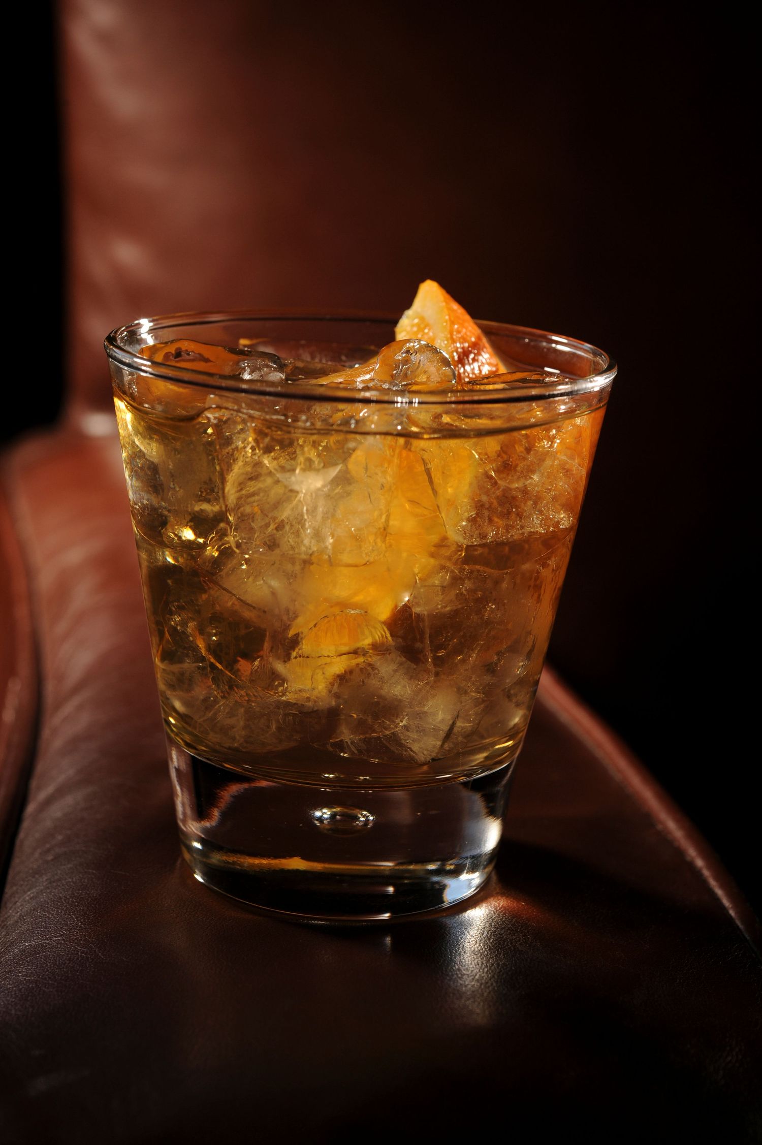 A classic whiskey cocktail on the rocks with an orange peel garnish in a lowball glass on a leather surface.