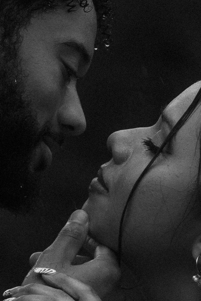 Black and white romantic close-up of a couple almost kissing, man gently holding womans chin tenderly.