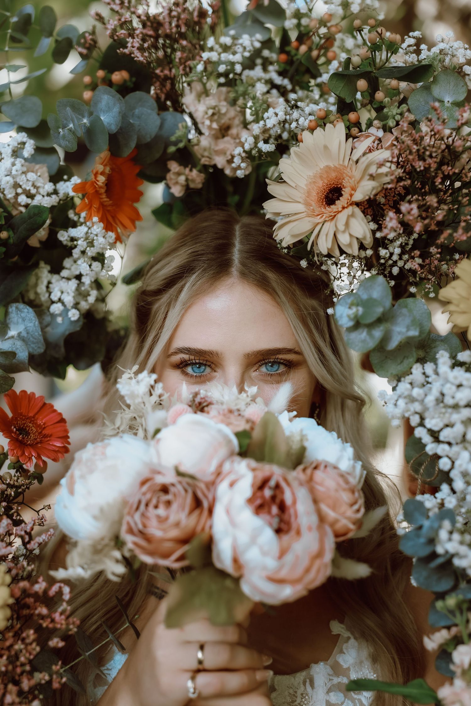 Blue-eyed blonde woman holding a bouquet of pink roses surrounded by colorful flowers including gerbera daisies.