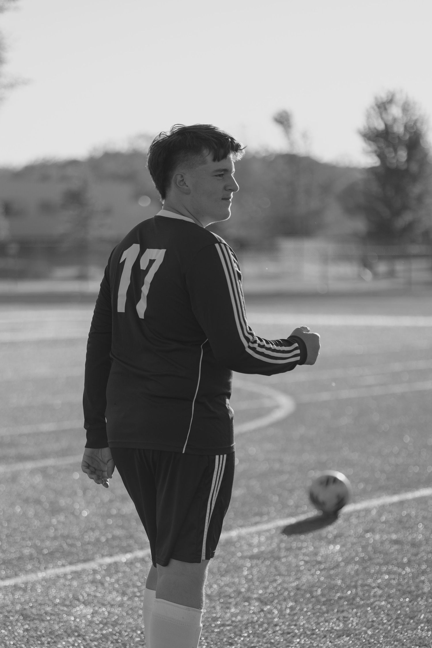 Black and white photo of soccer player #17 in Adidas uniform standing on outdoor field.
