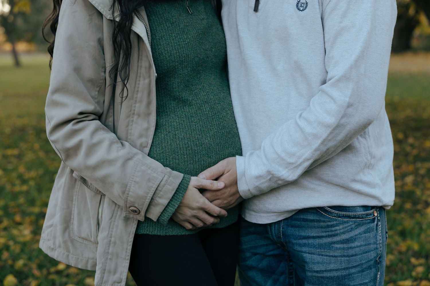 Close-up of couple holding hands tenderly in an autumn park with golden leaves in background.