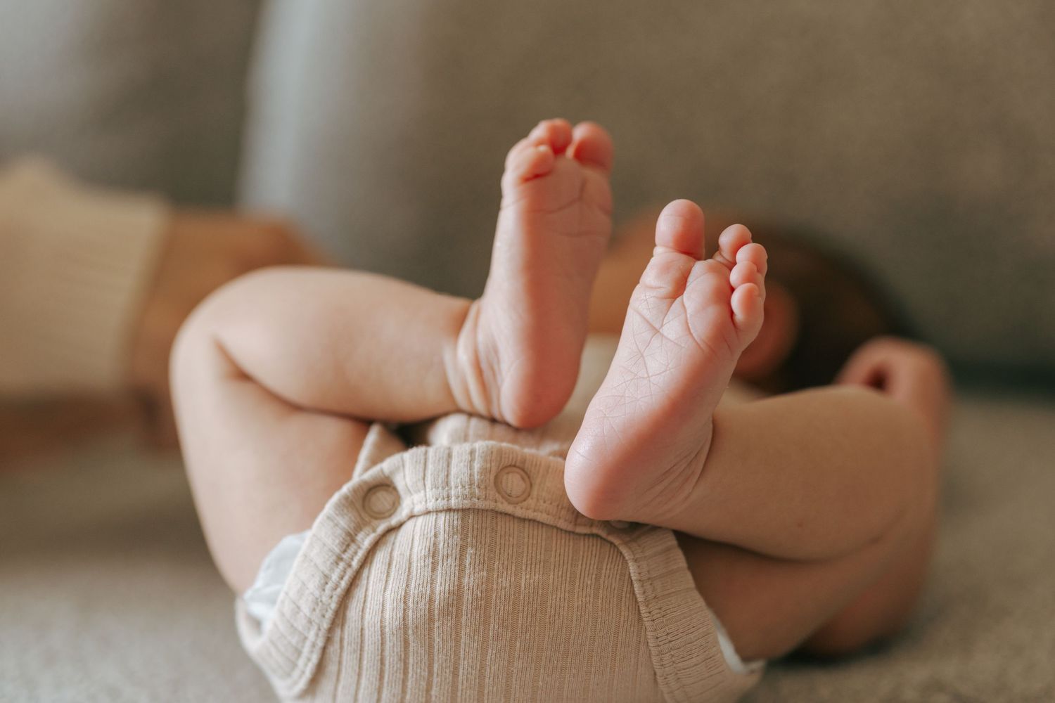 Close-up of tiny newborn baby feet and legs resting on soft neutral colored blanket.