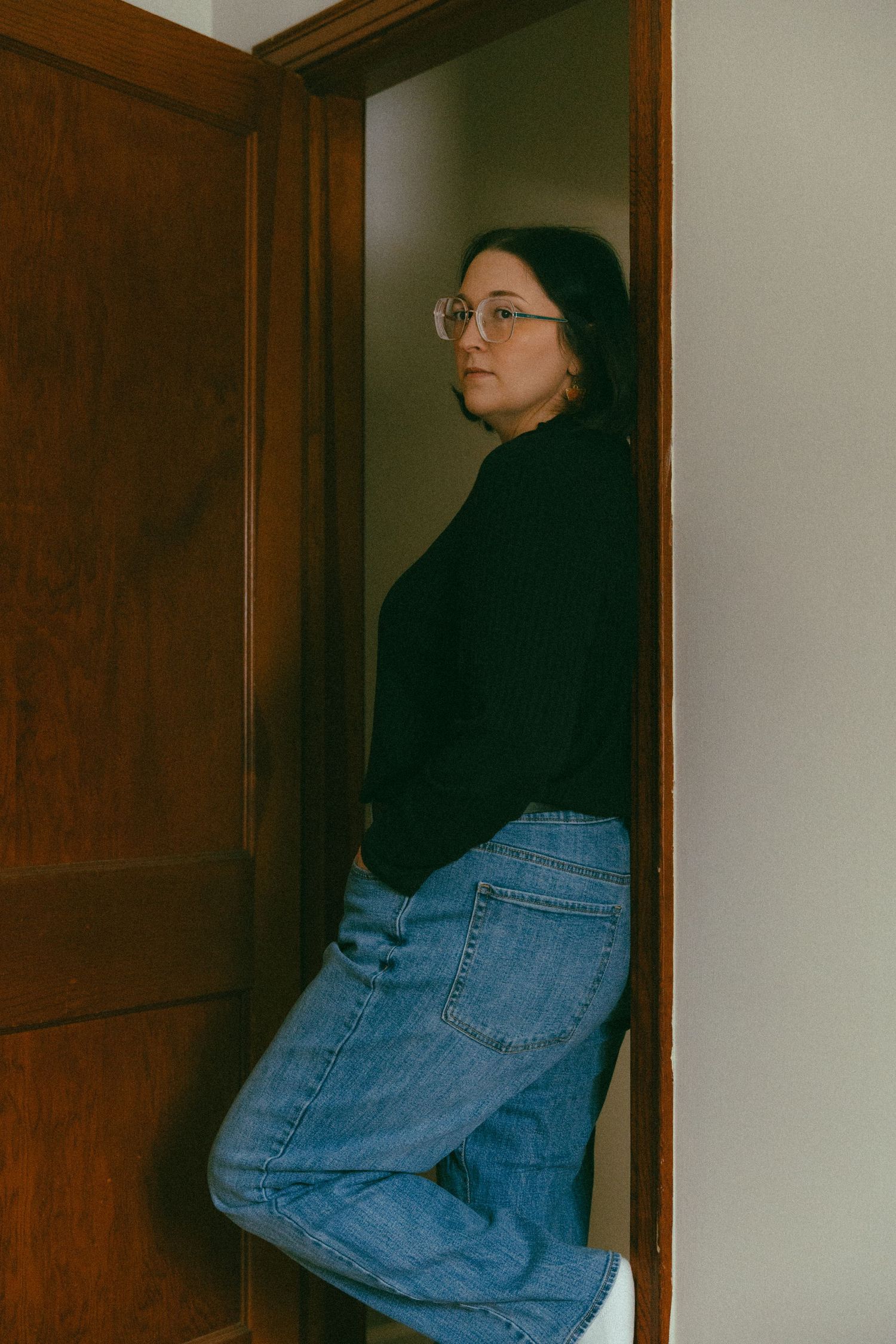 Stylish woman with glasses in black turtleneck and wide-leg jeans by wooden door.