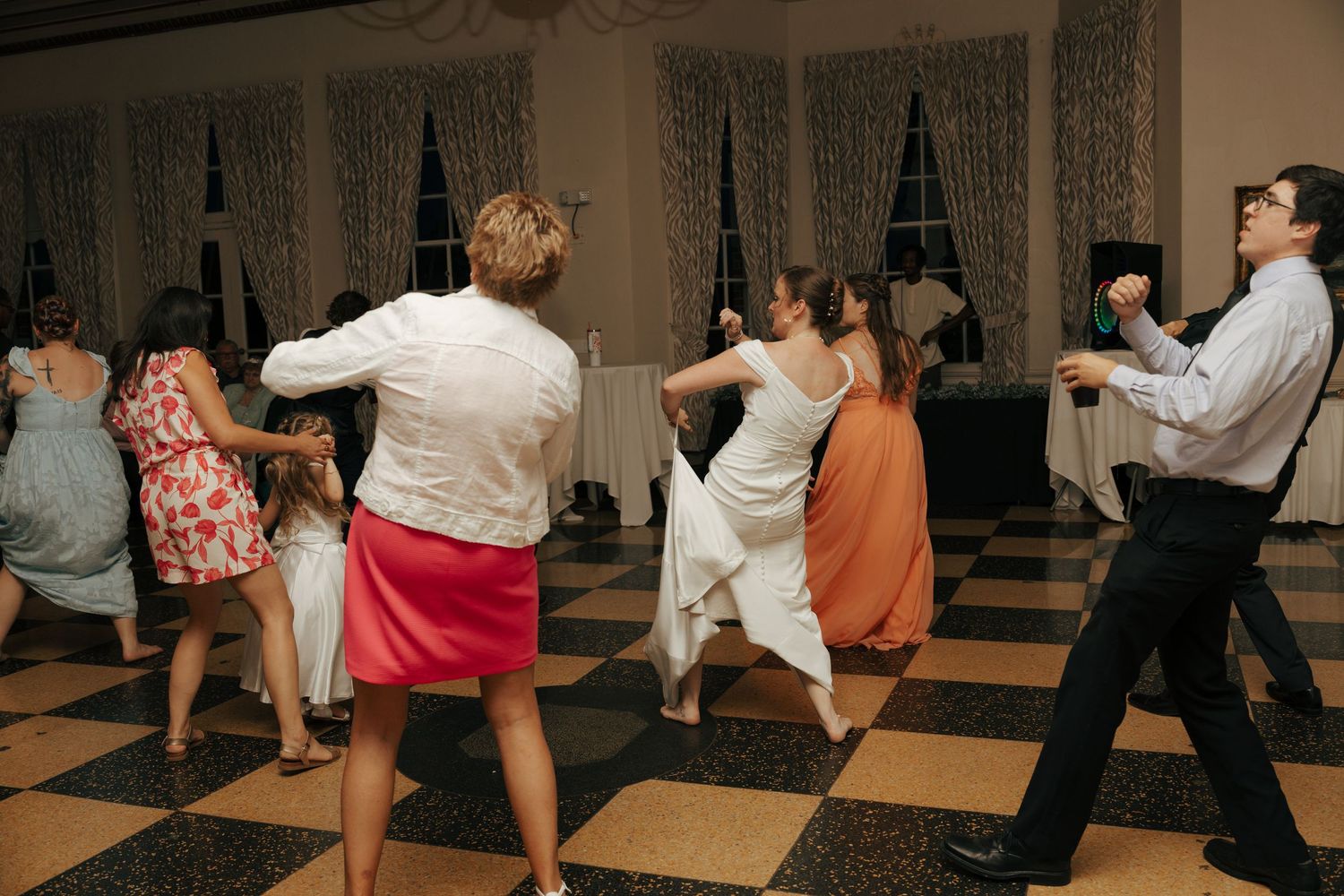 Wedding guests dancing joyfully on a classic checkered dance floor at a reception.