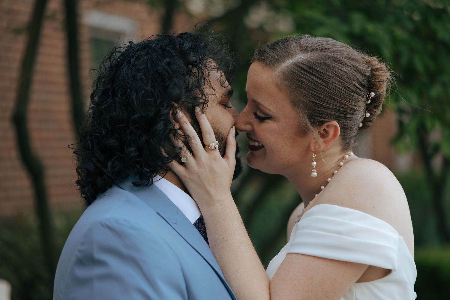 Bride and groom sharing a romantic almost-kiss moment outdoors, bride cupping grooms face tenderly.