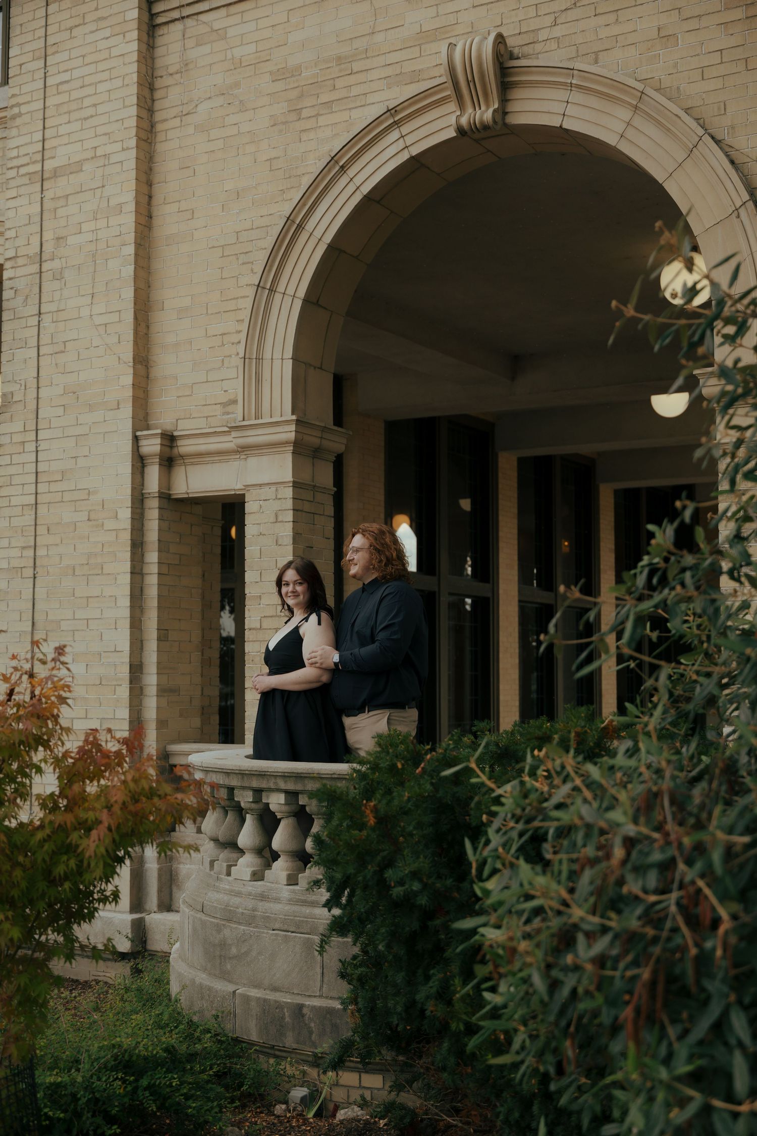 Couple standing together on an ornate stone balcony of a historic building.