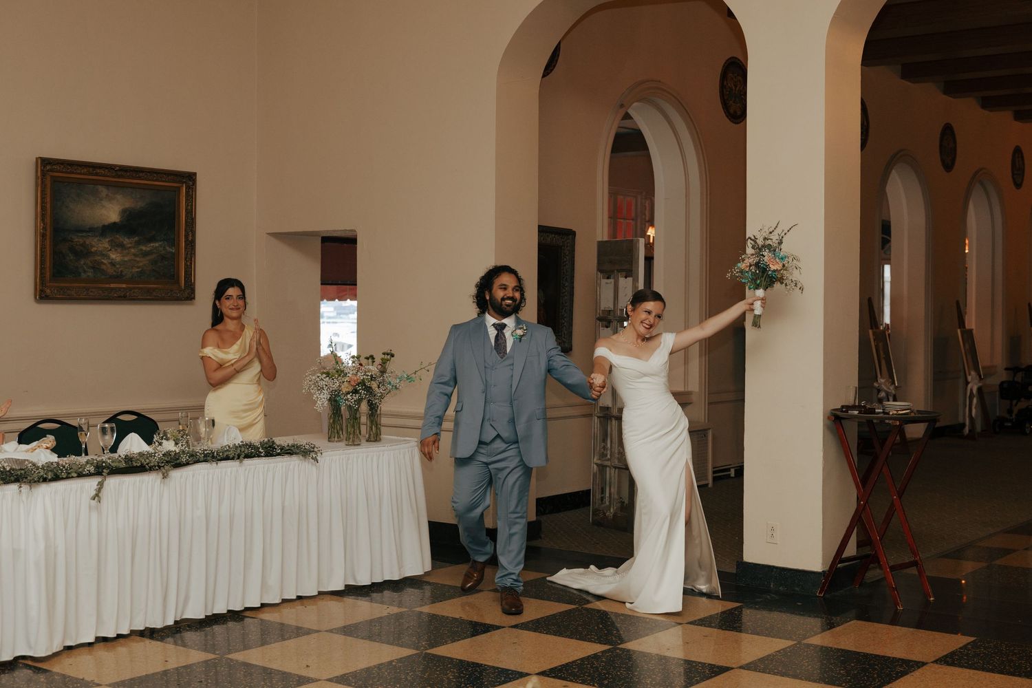 Bride and groom making grand entrance into elegant wedding reception hall with checkered floors.