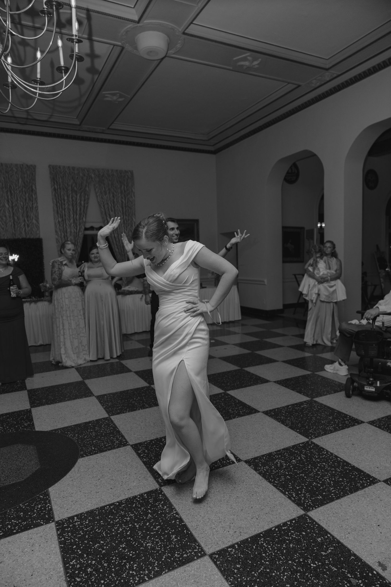 Black and white photo of bride dancing elegantly on checkered floor at wedding reception.