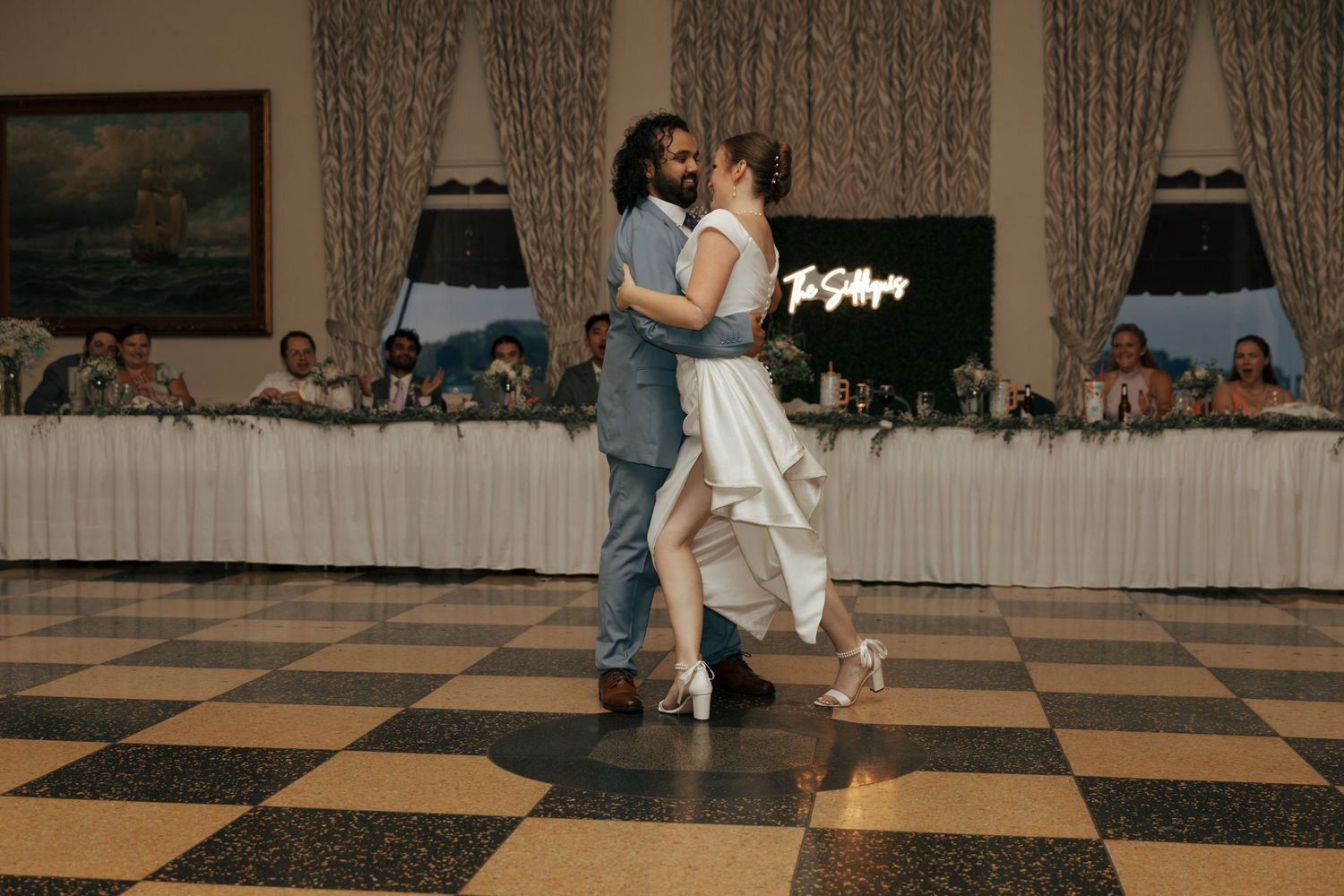 Bride and groom sharing romantic first dance on classic black and white checkered ballroom floor.