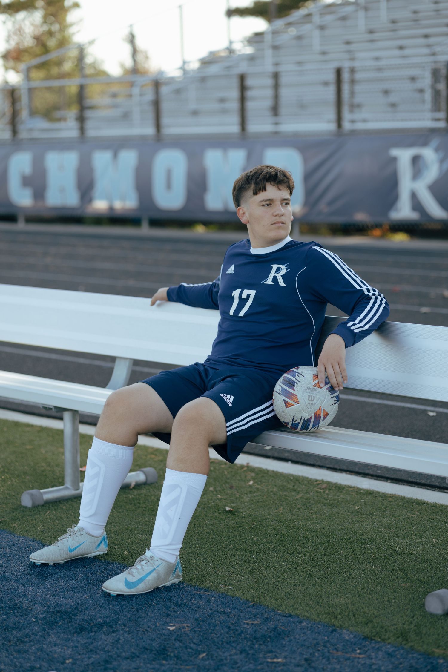 High school soccer player #17 poses on bench with ball in navy Adidas kit at Richmond field.