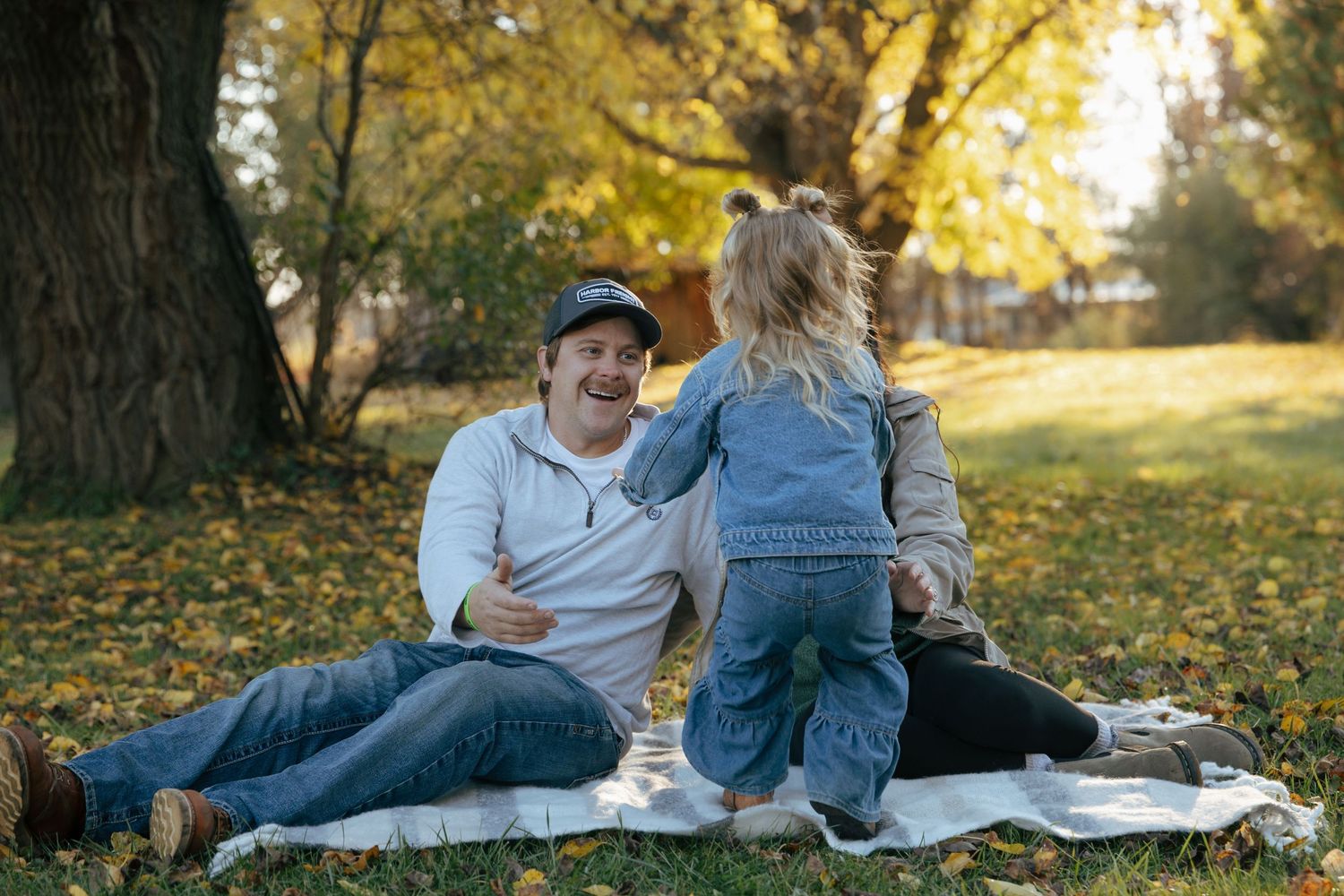 Man and young girl enjoying autumn picnic on blanket under colorful fall trees in park.