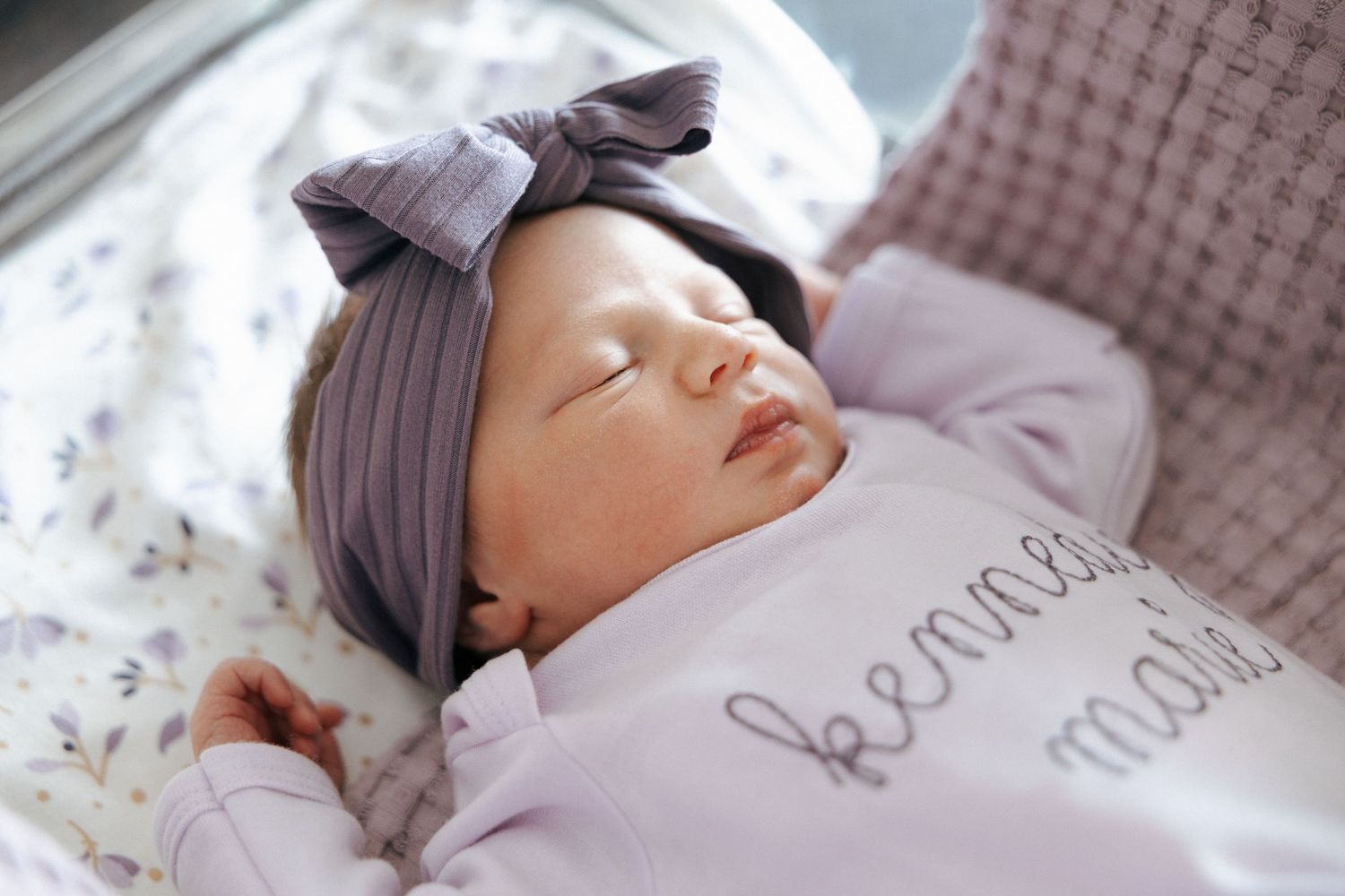 Sleeping newborn baby girl in purple outfit and bow headband named Kennedy Marie.
