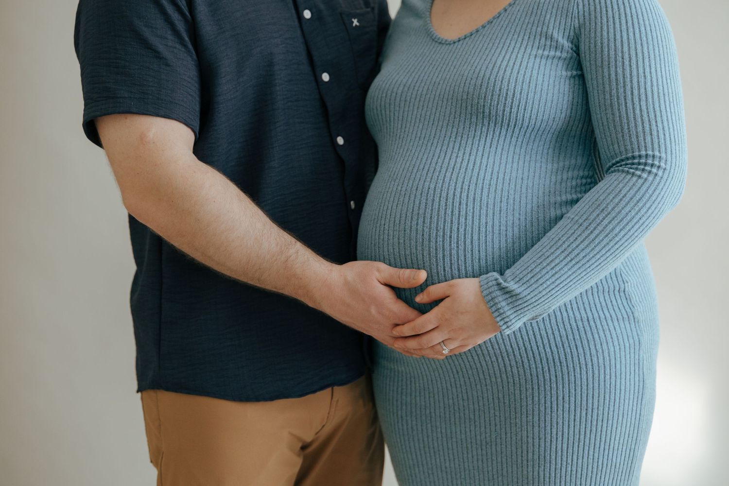 Couple tenderly cradles a baby bump together in a minimalist maternity portrait session.