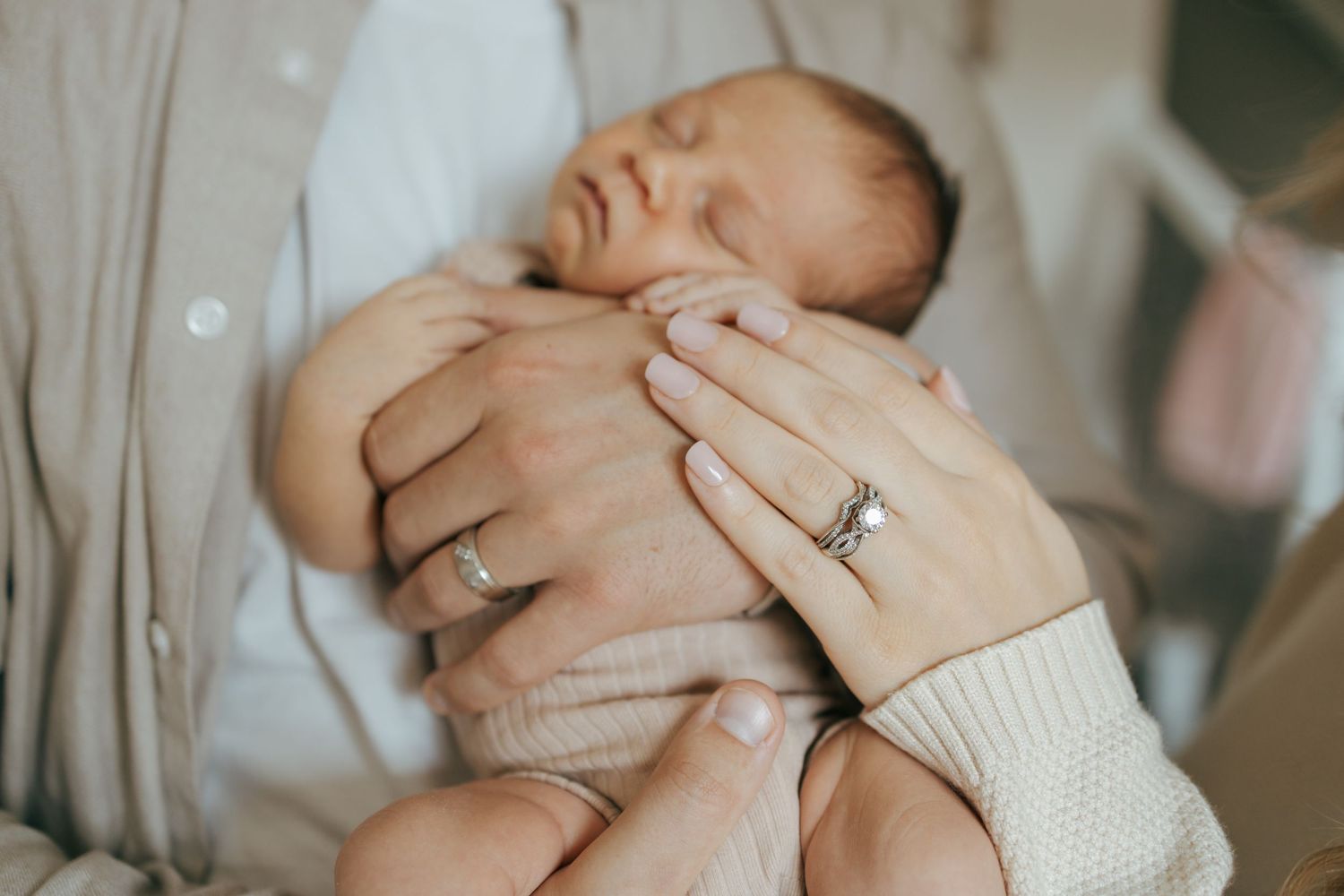 Close-up of sleeping newborn baby cradled in parents hands showing wedding and engagement rings.