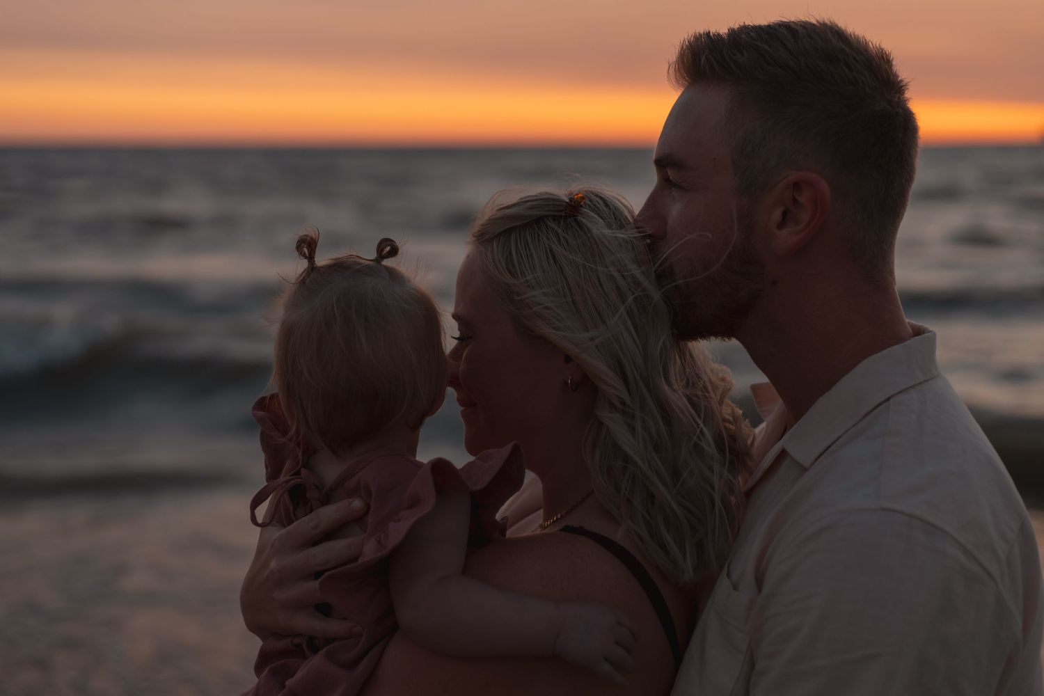 A couple sharing a tender moment with their baby daughter at a beautiful beach sunset.