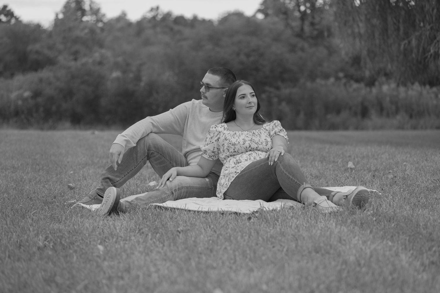Black and white photo of couple relaxing together on blanket in open grass field.