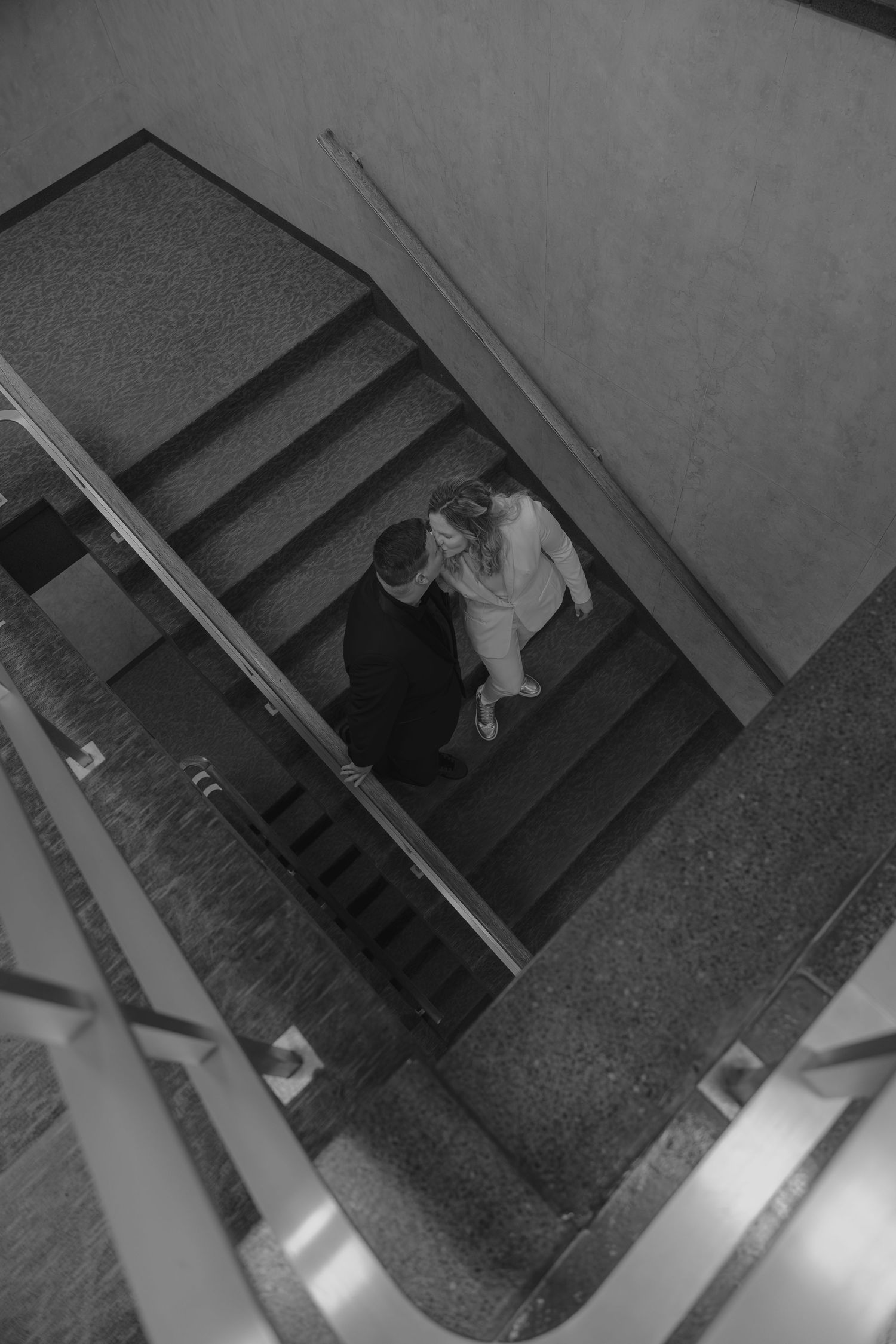 Aerial black and white view of a couple embracing on a staircase in a modern building.