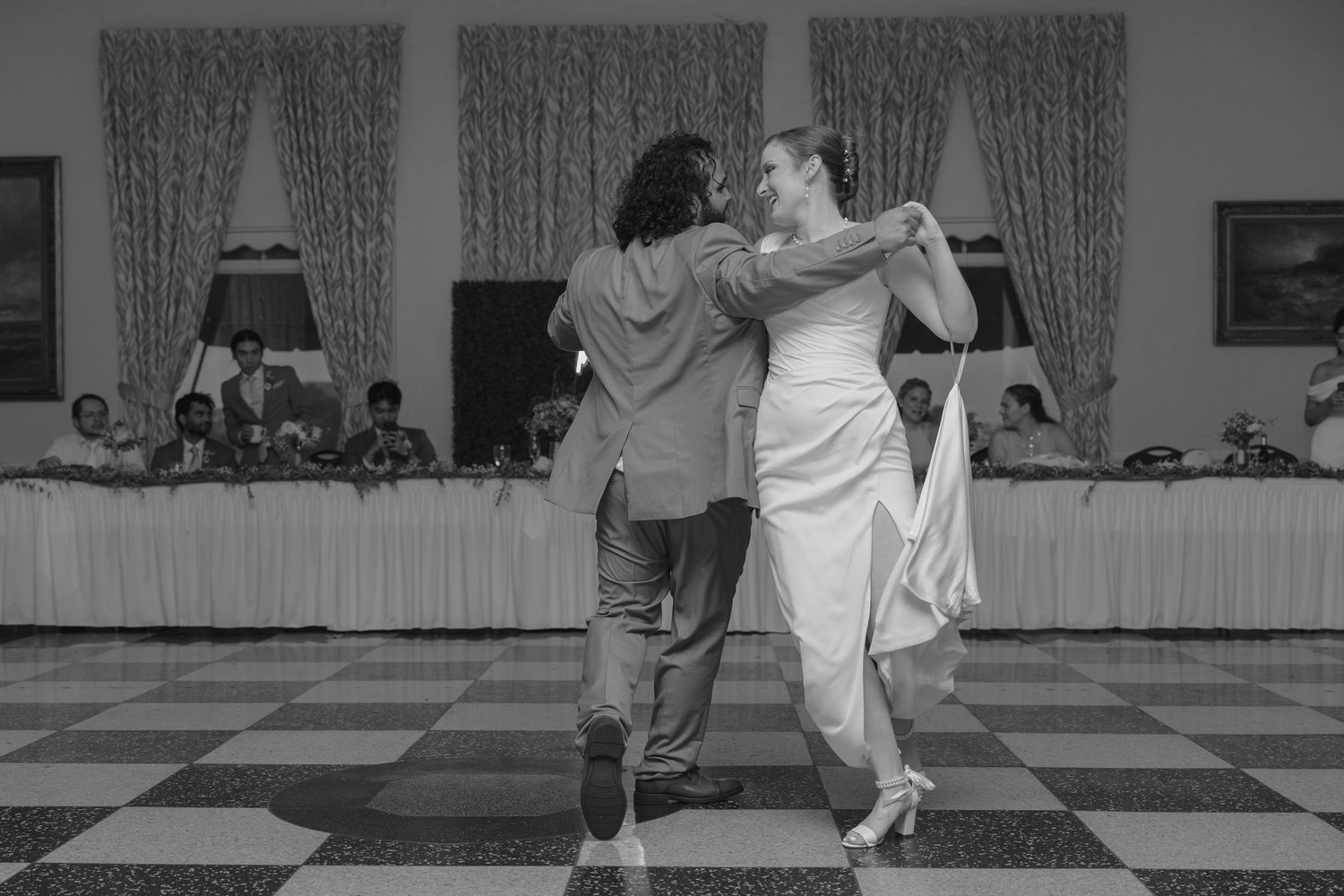 Black and white photo of bride and groom dancing together at elegant wedding reception.