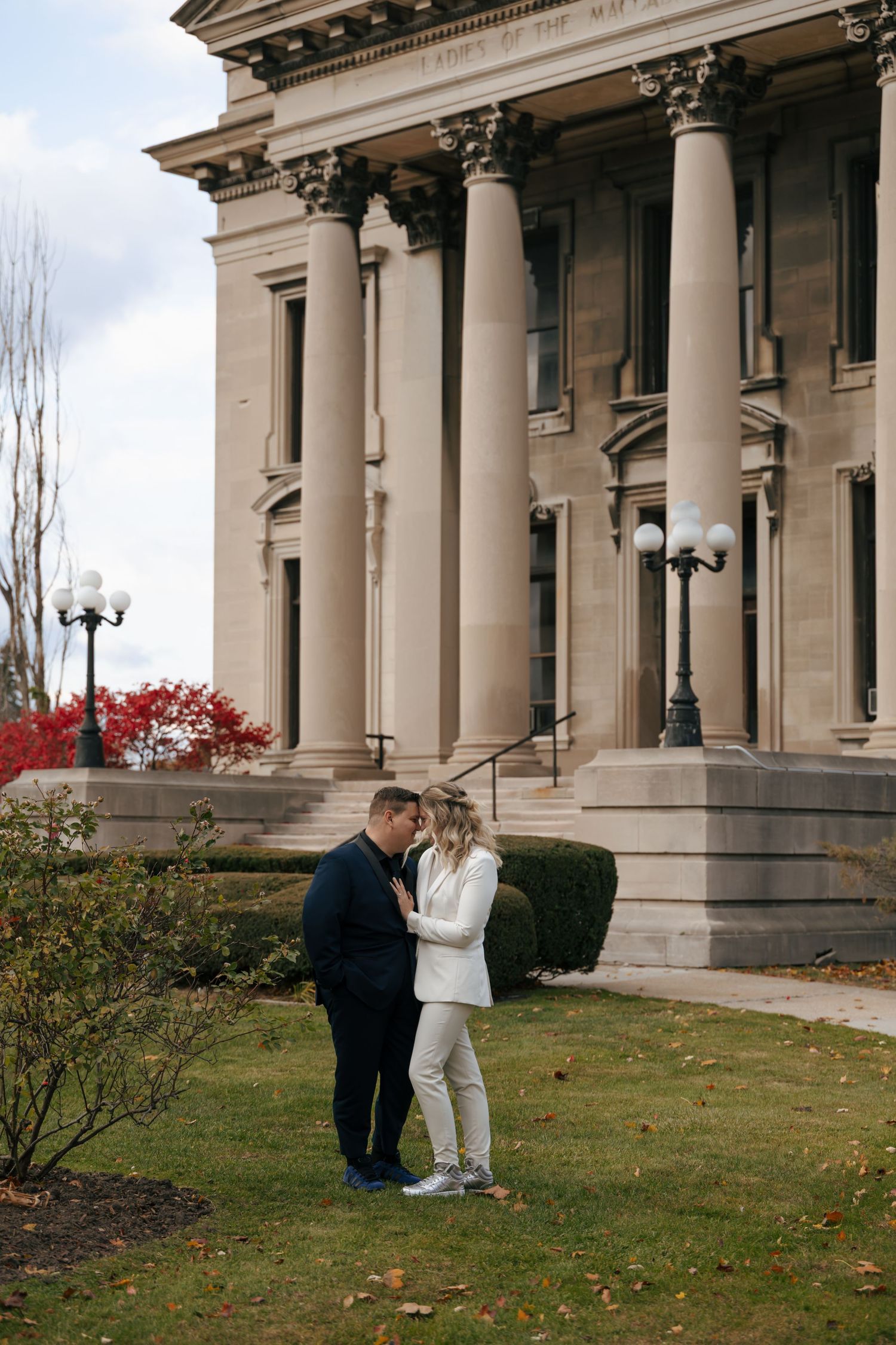 Couple sharing a romantic moment in front of a grand neoclassical building with tall columns during fall.